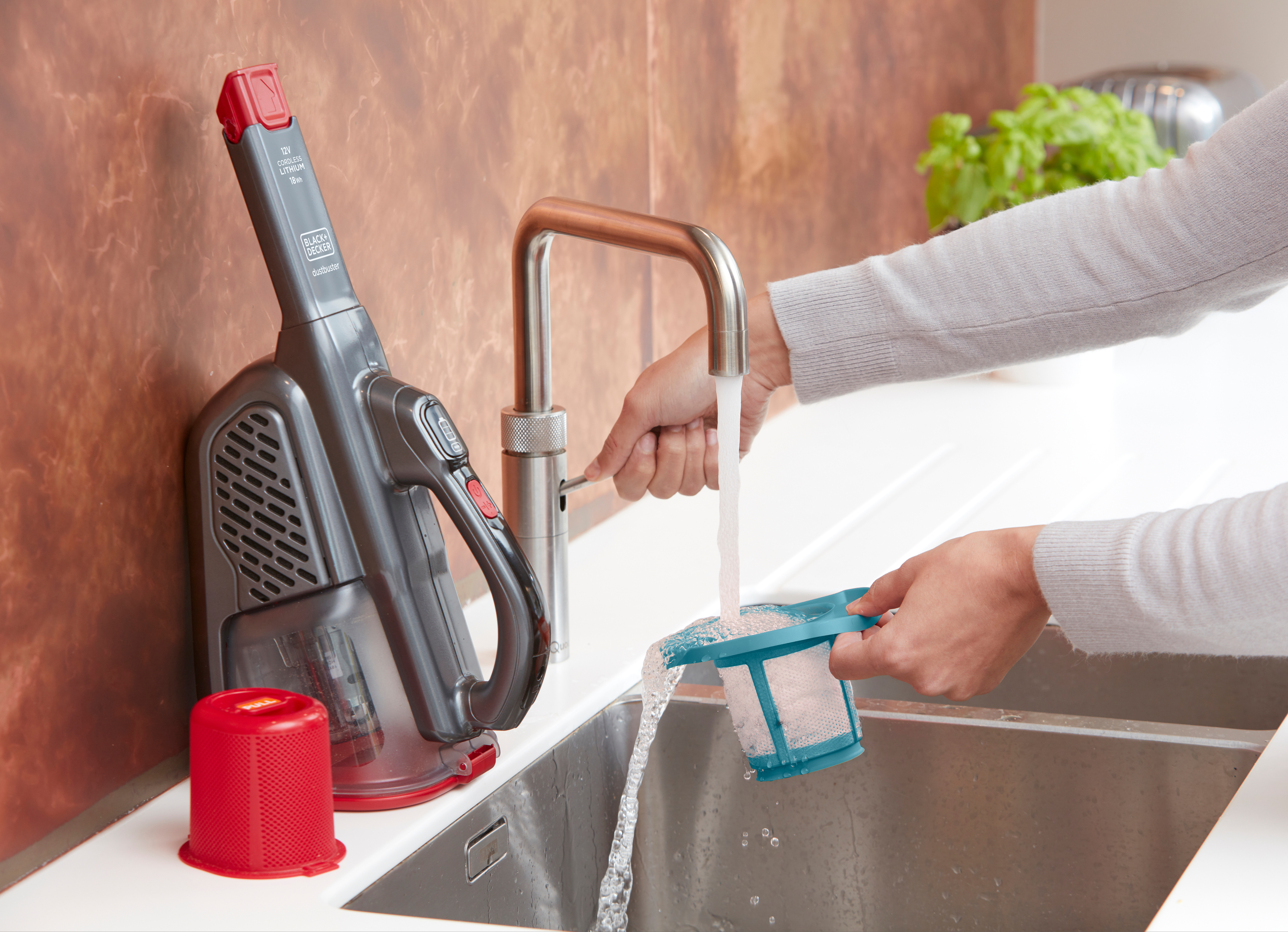 Eine Person reinigt einen Staubsaugerfilter am Küchenbecken.