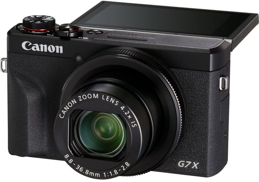 A black Canon G7X camera with a lens and a pop-up screen. The background is white.