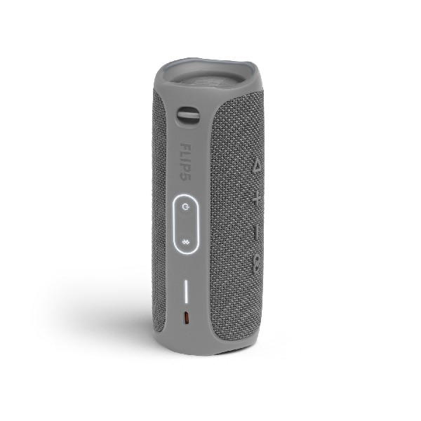 Un altavoz gris JBL Flip 5. Es cilíndrico con botones y un puerto de carga.