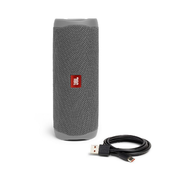 Un altavoz portátil JBL gris con un cable de carga negro. El altavoz está sobre un fondo blanco.