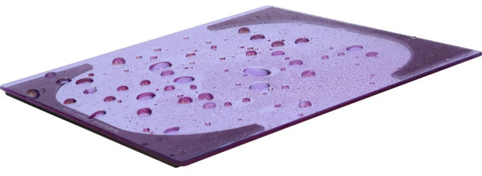 Purple glass cutting board with water drops on a white background.