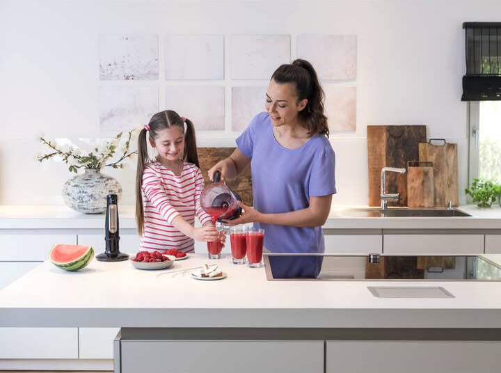 Mutter und Tochter machen Smoothies. Sie stehen an einer Kücheninsel mit Obst.