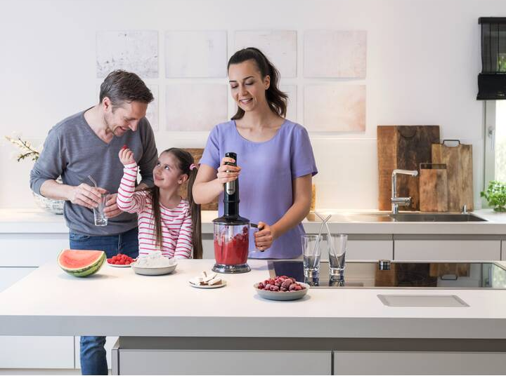 Familie macht Smoothie. Mann, Frau und Kind in der Küche. Mixer in Gebrauch. Beeren.