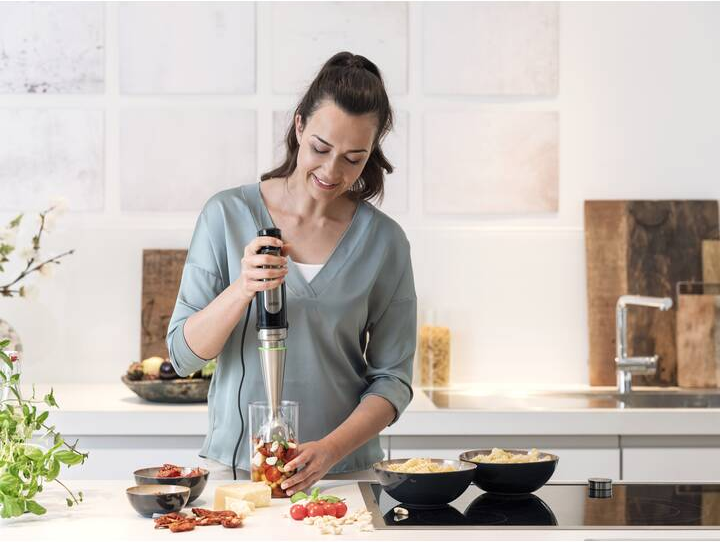 Frau mixt Tomaten mit einem Stabmixer in einer Küche.