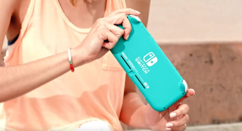 Una persona sosteniendo una Nintendo Switch Lite de color verde azulado. La parte trasera de la consola es visible.