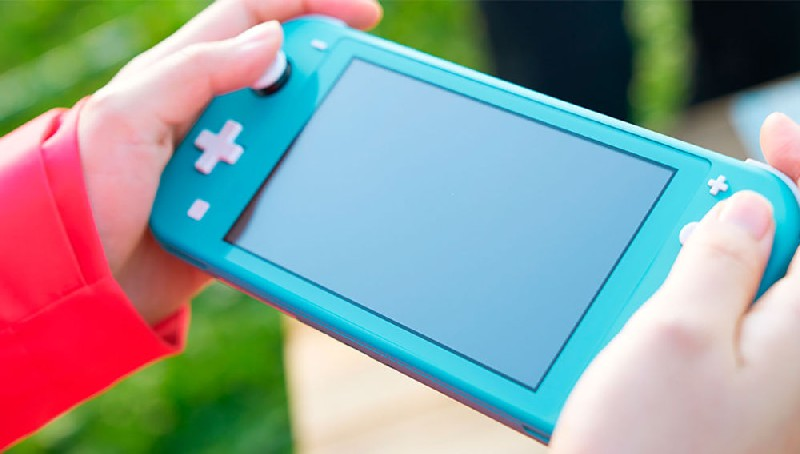 Manos sosteniendo una Nintendo Switch Lite turquesa. Los botones son rosa y blanco.
