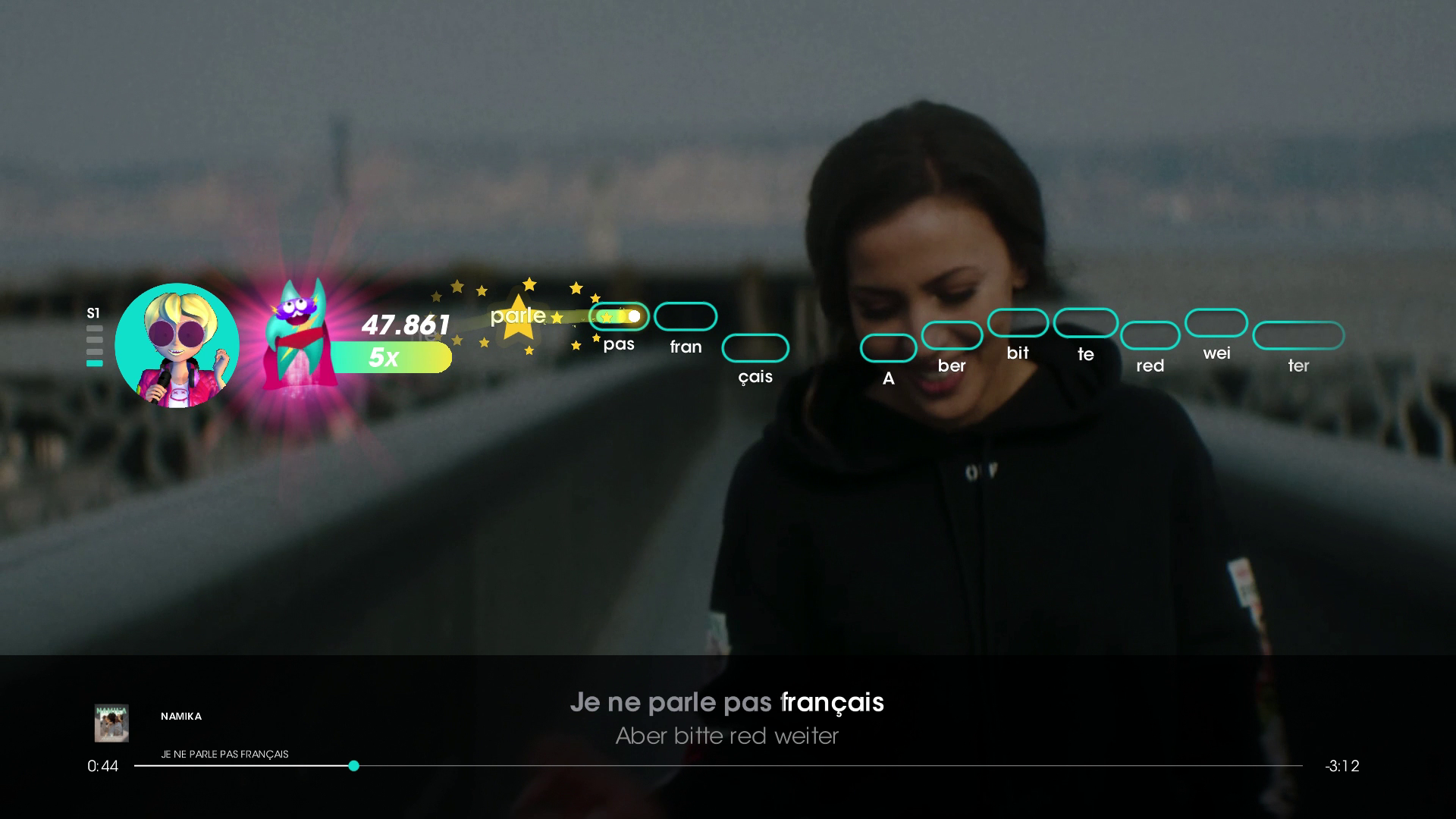 Una donna canta sul palco, con i testi visualizzati. Un'interfaccia di gioco è visibile. Il testo appare in francese.