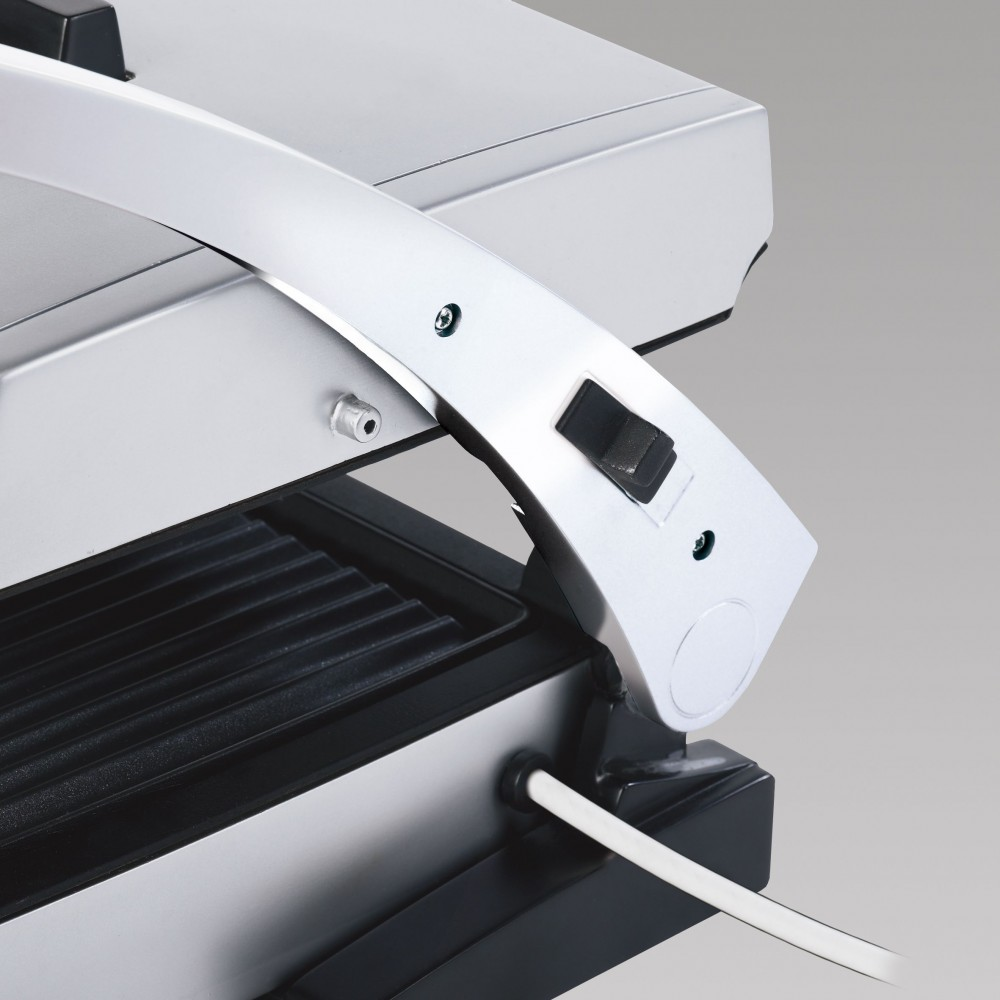 Close-up of a silver grill press with a black cooking surface and a white cord.
