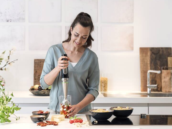Frau, die Tomaten mit einem Stabmixer in einer Küche mixt.