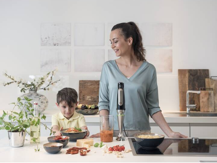 Frau und Kind in einer Küche, die mit einem Handmixer Essen mixen.