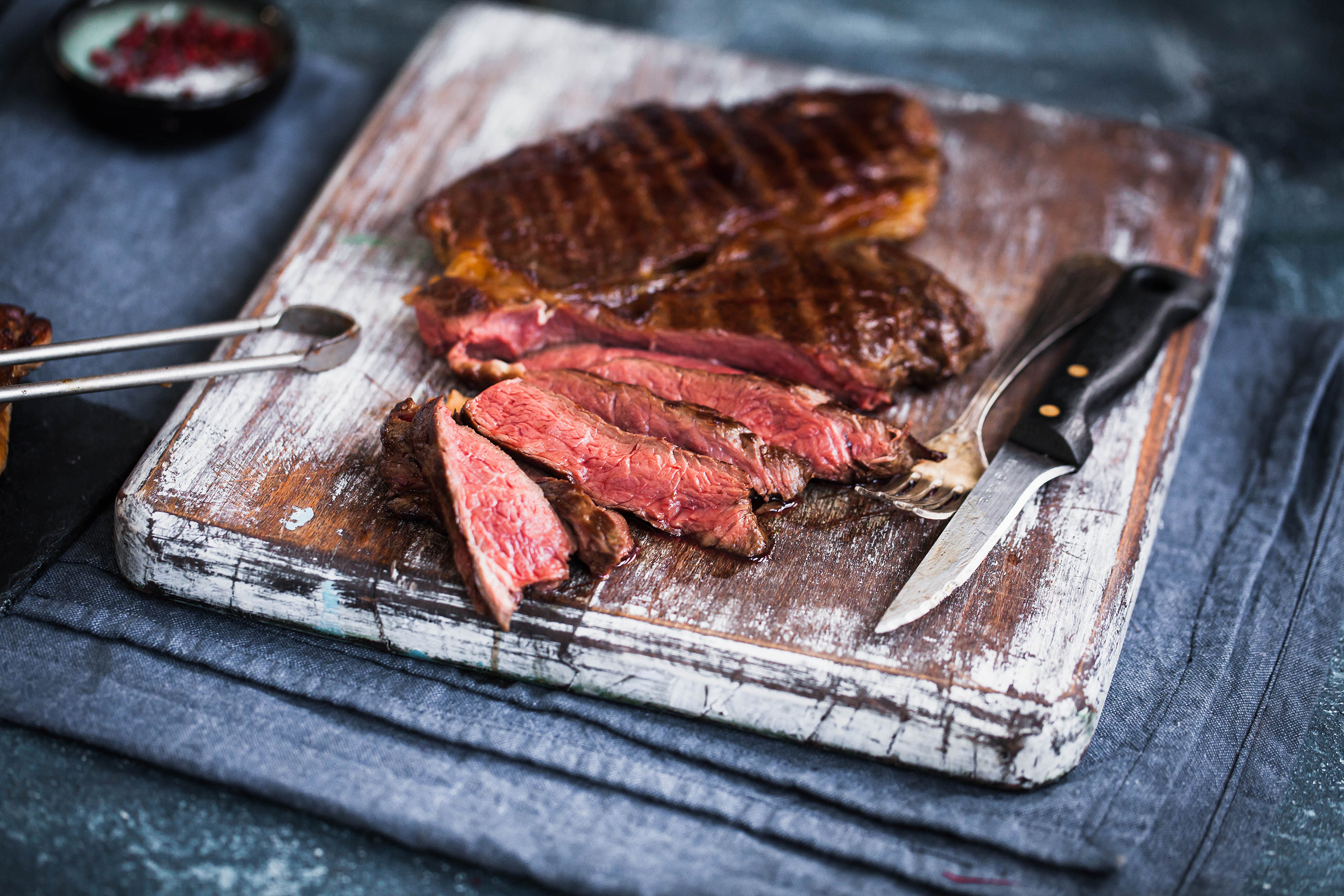 Geschnittenes Steak auf einem Holzbrett mit Messer und Gabel, rotes Fleisch sichtbar. Nahaufnahme.