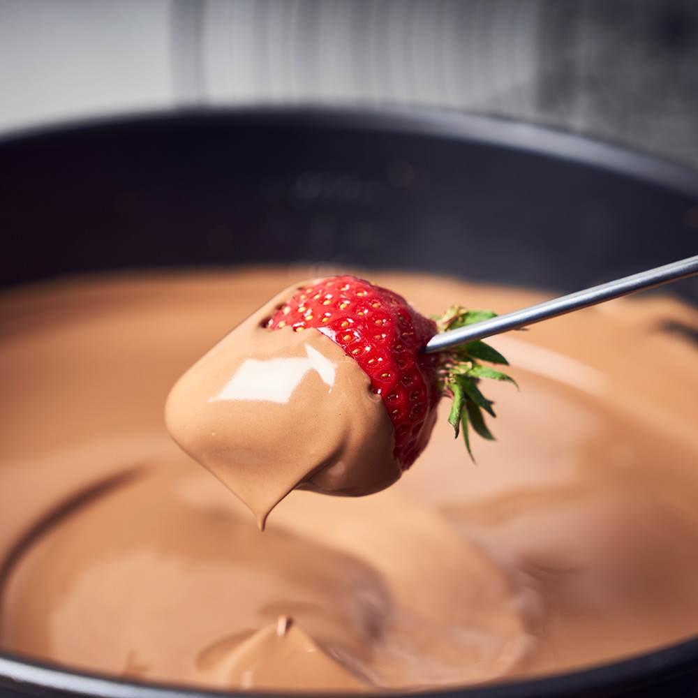 Erdbeere in Schokolade getaucht, am Stiel, über einem Fondue-Topf.