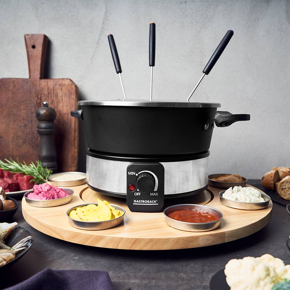Fondue-Set mit schwarzem Topf, Holzsockel mit Dip-Schalen und einem Bedienknopf.