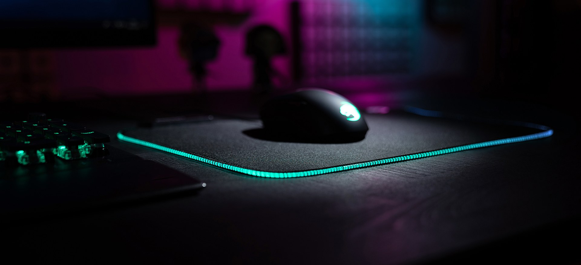 Configuration de jeu avec souris et tapis de souris à bordure néon. Clavier à gauche. Bureau noir, scène sombre.