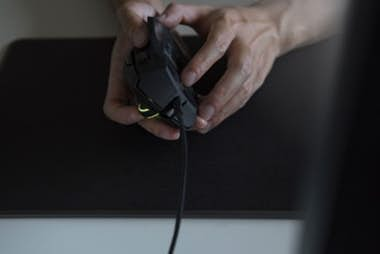 Manos sosteniendo un ratón de juego negro sobre una alfombrilla negra.