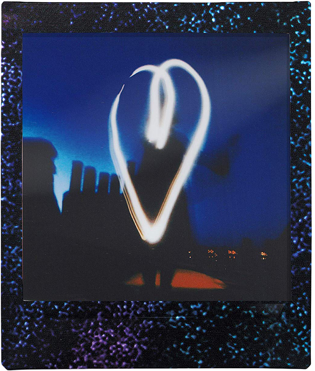 Polaroid fotó fehér fény szívvel kék háttéren, város sziluettjével.