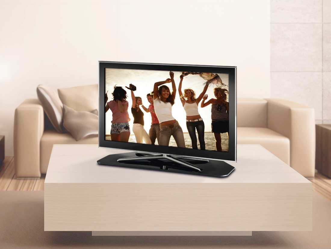 Uno schermo TV mostra un gruppo di persone che ballano su una spiaggia. Un divano beige è dietro la TV.