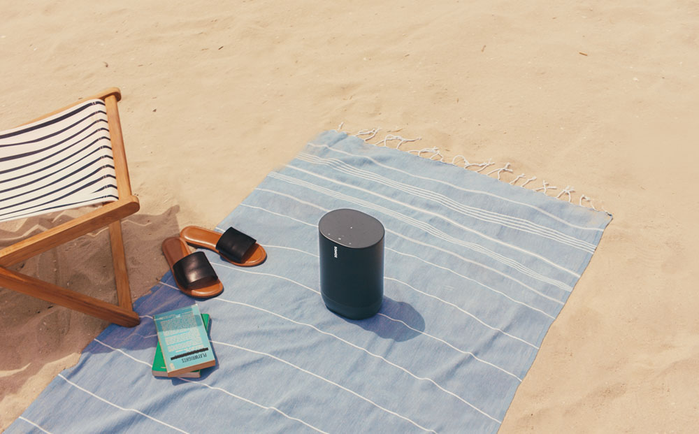 Strandscène met een luidspreker, handdoek, sandalen en boeken. Zand op de voorgrond.