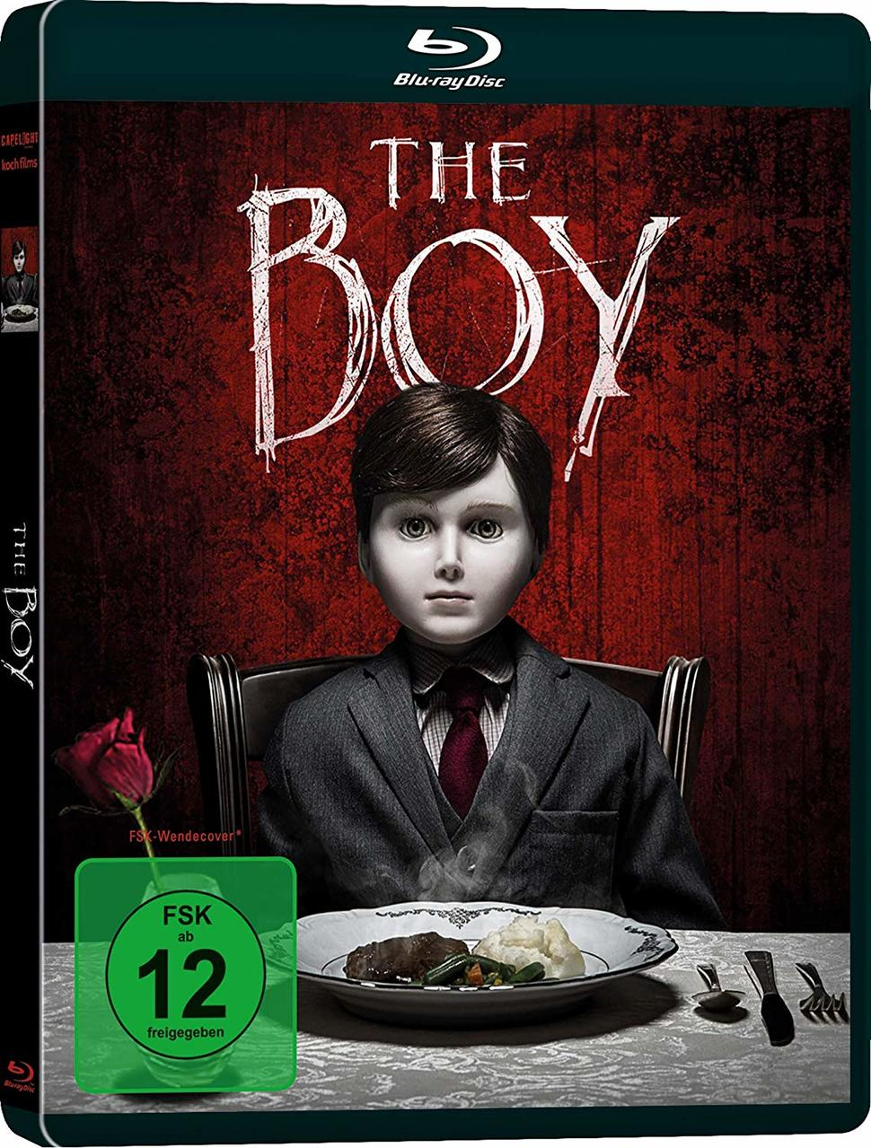 Filmcover von 'The Boy': Eine Puppe im Anzug sitzt an einem Tisch, mit dunklem roten Hintergrund.