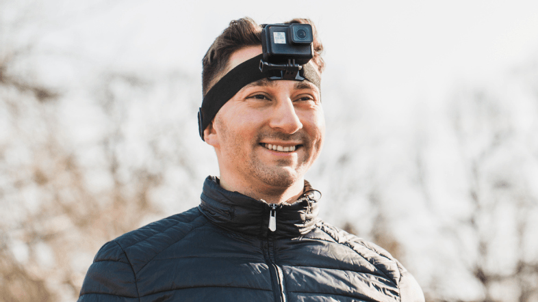 Homme portant une caméra d'action fixée sur la tête, souriant à l'extérieur.