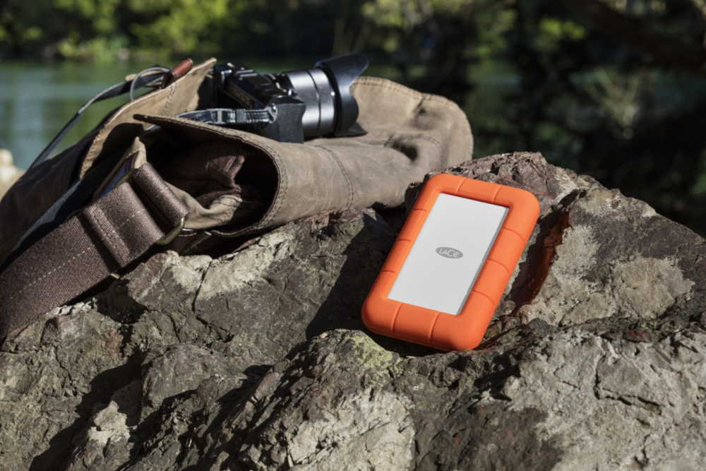 Orange rugged case with a white rectangle on a rock, camera bag, and camera.