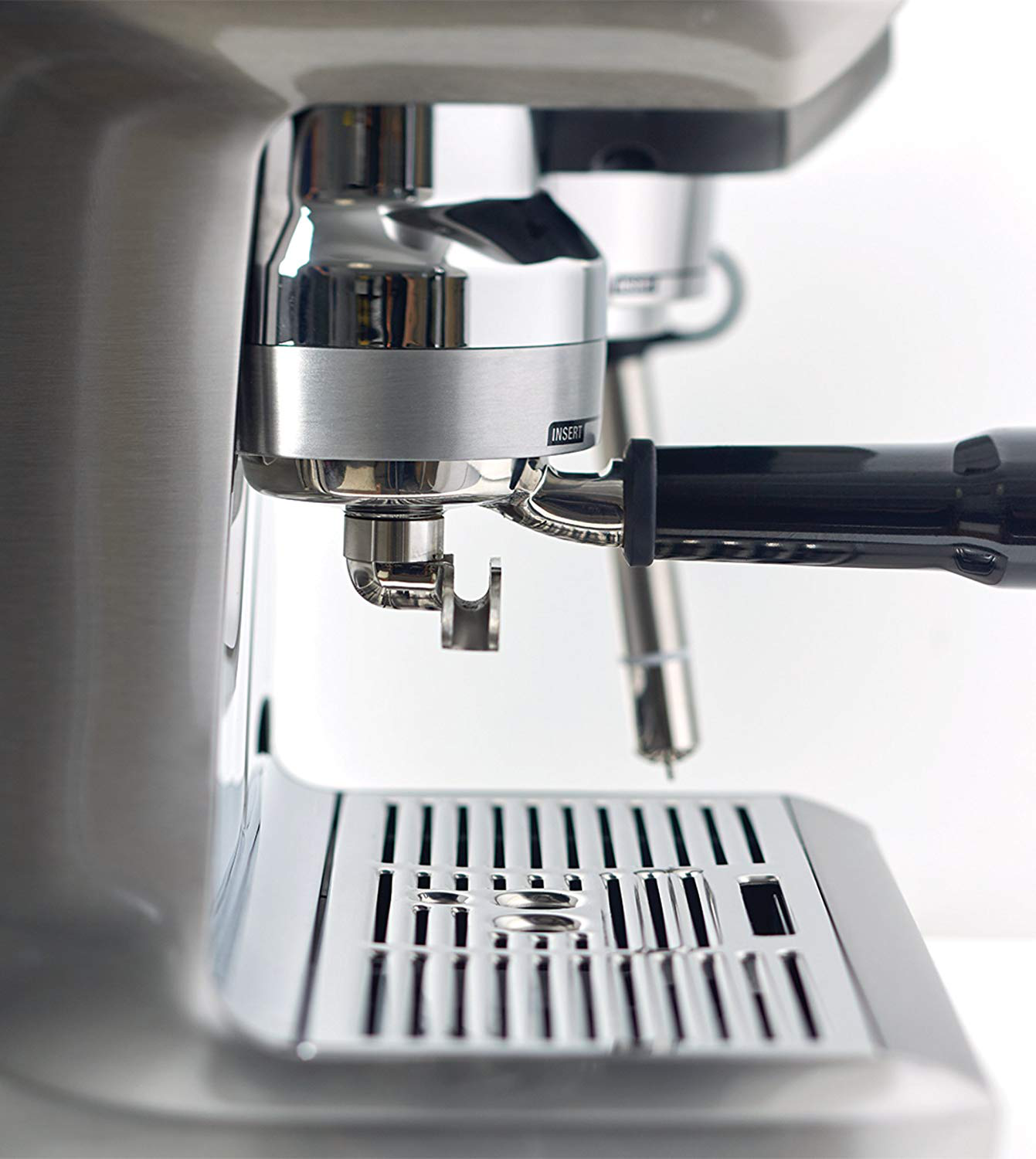Gros plan sur une machine à expresso en acier inoxydable. Le porte-filtre est en place, et une poignée noire est visible. Un bac d'égouttement en bas.