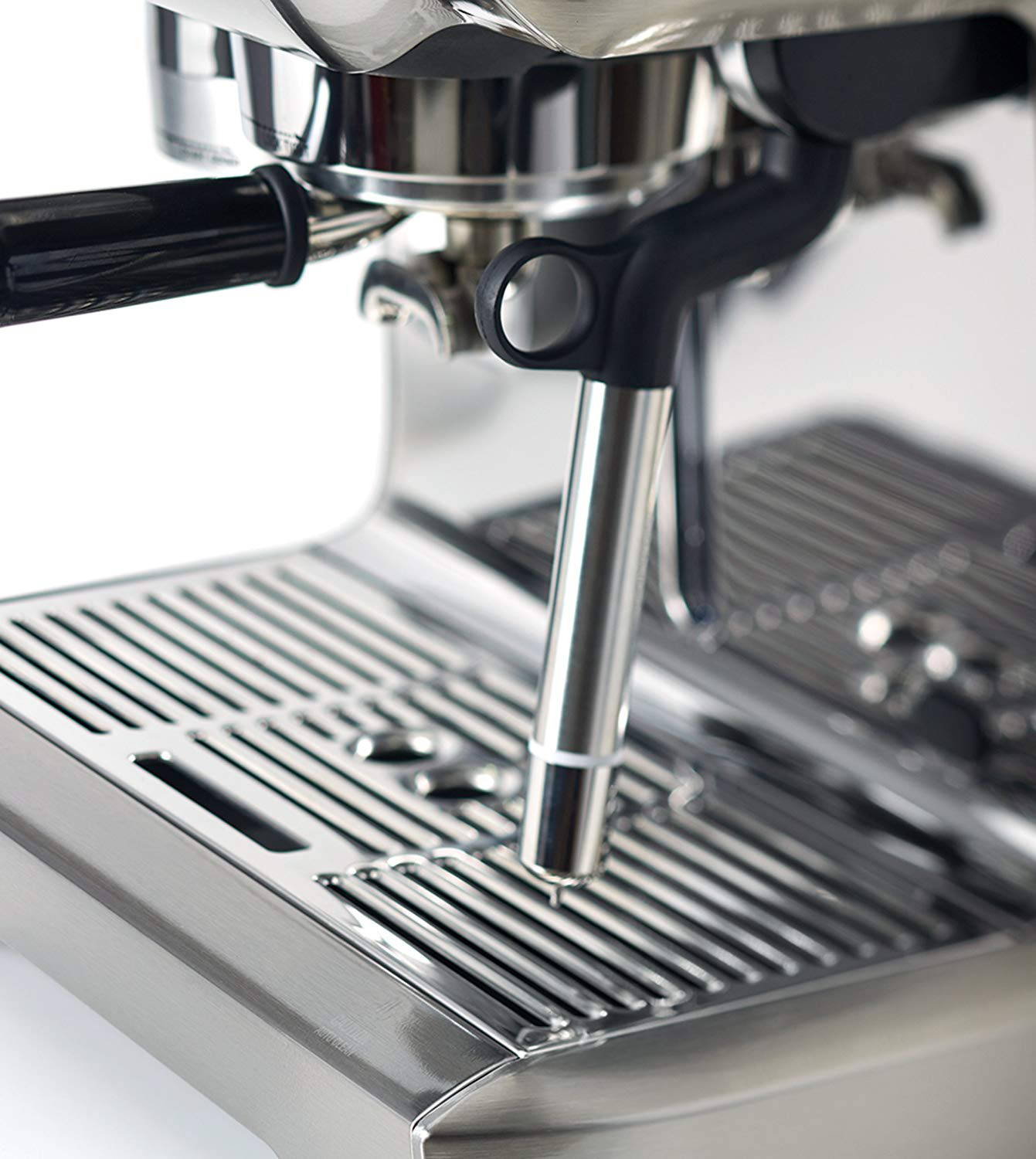Gros plan sur une machine à expresso en acier inoxydable avec une poignée noire et un bac d'égouttement en métal. Le fond est blanc.
