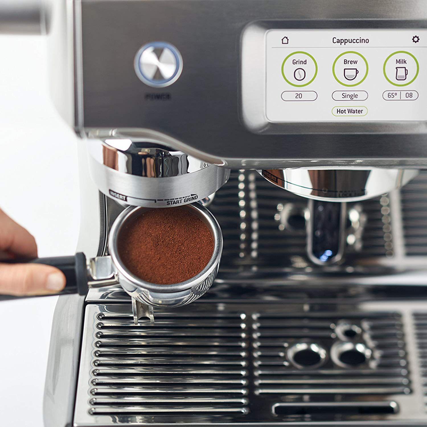 Une machine à expresso argentée avec écran, porte-filtre avec café moulu et une main tenant le porte-filtre.