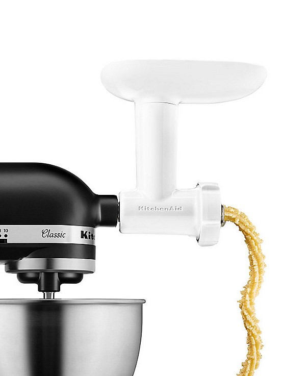 Ein weißer KitchenAid-Aufsatz zur Herstellung von Pasta, wobei Pasta extrudiert wird.