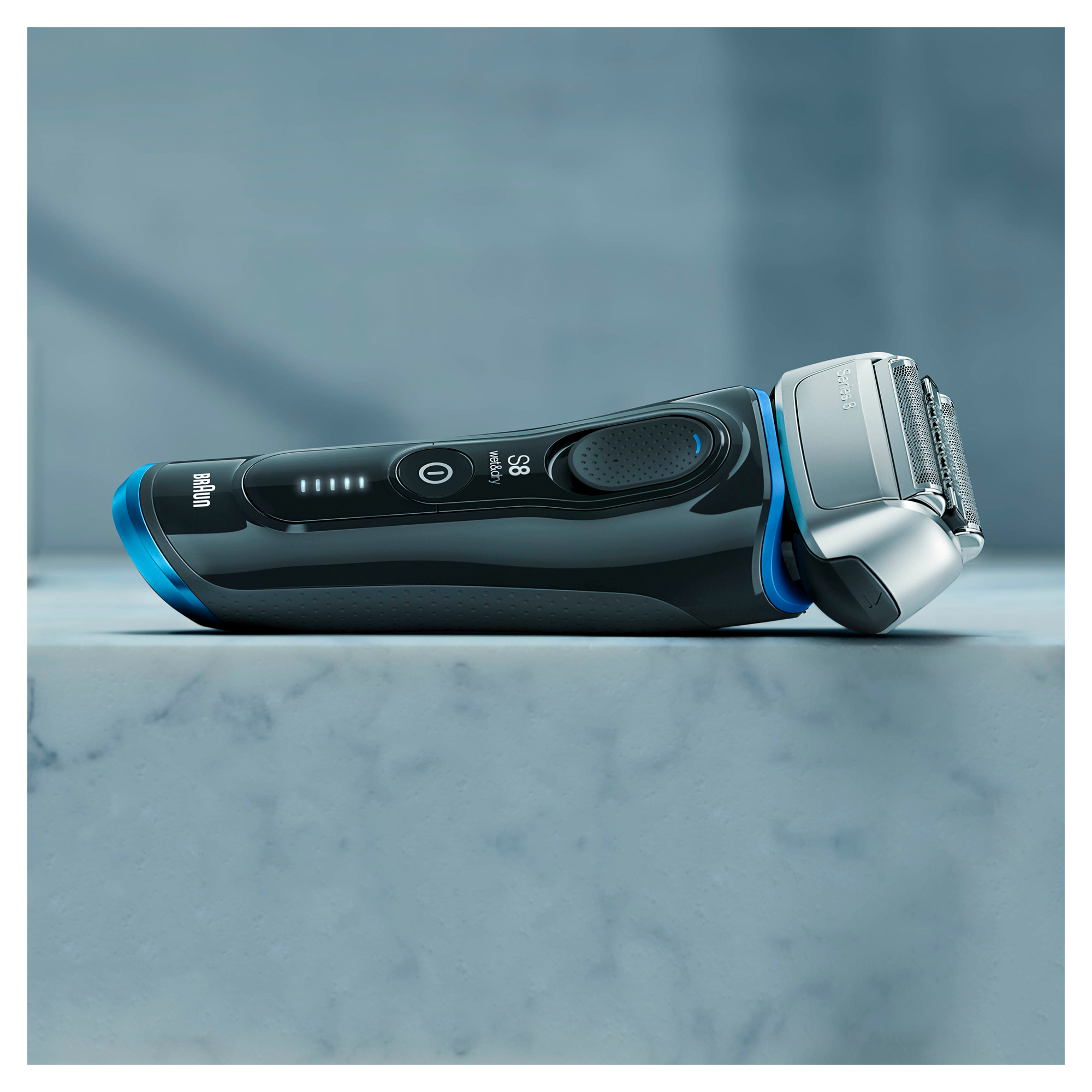 Black and blue Braun electric shaver on a marble surface, lit by blue light.