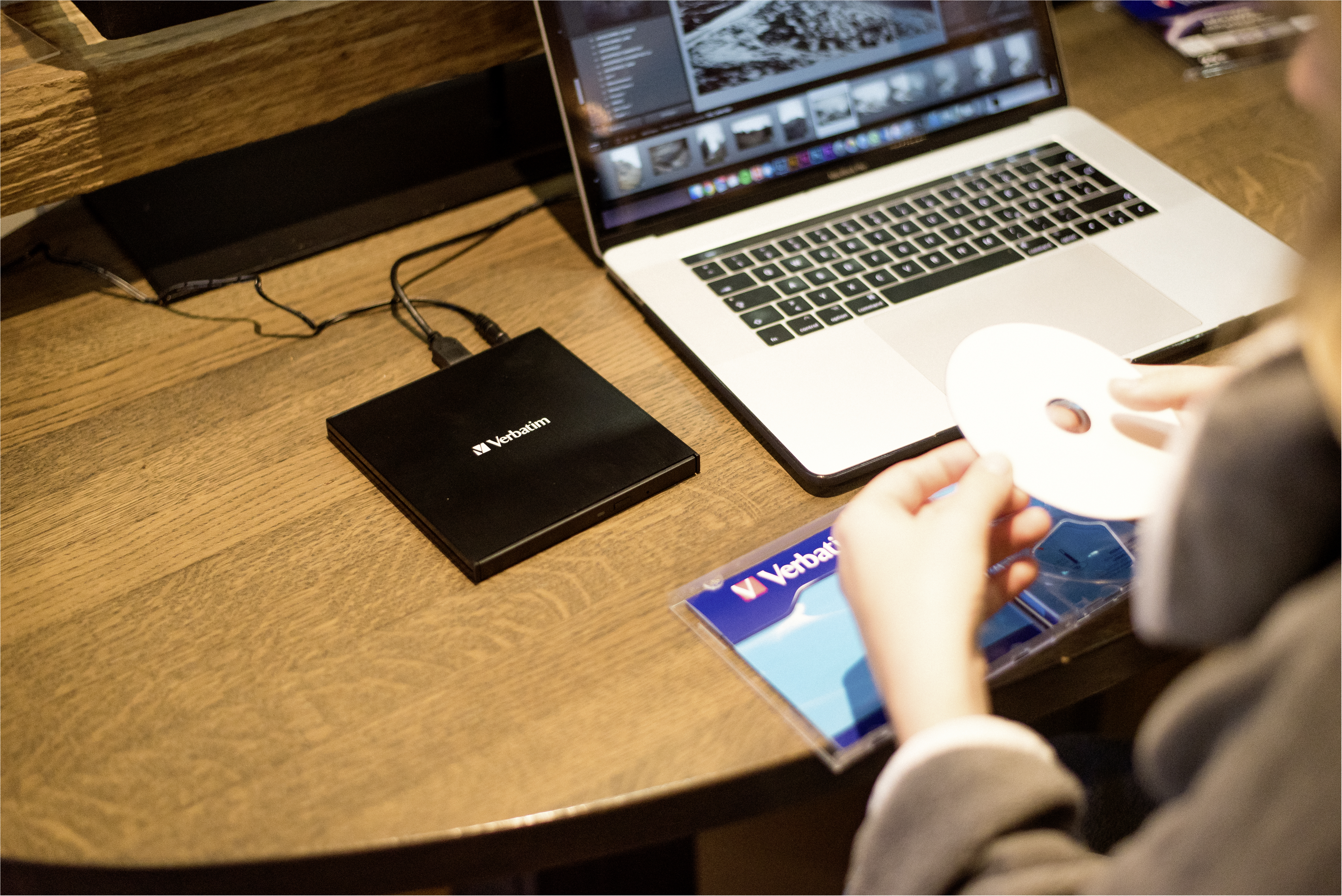 Laptop mit schwarzem externem Laufwerk daneben, CD und Person, die eine CD hält.