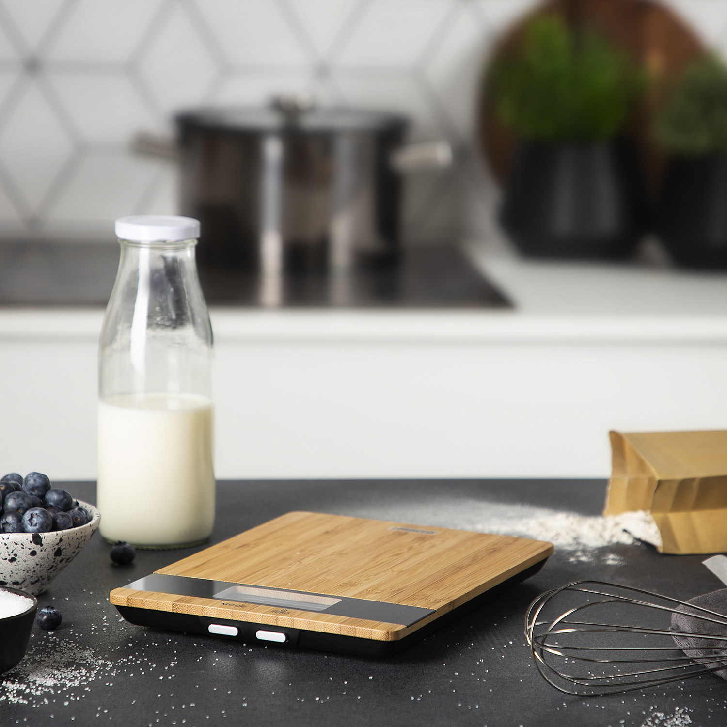 Kitchen scene with a wooden scale, blueberries, milk, and flour.