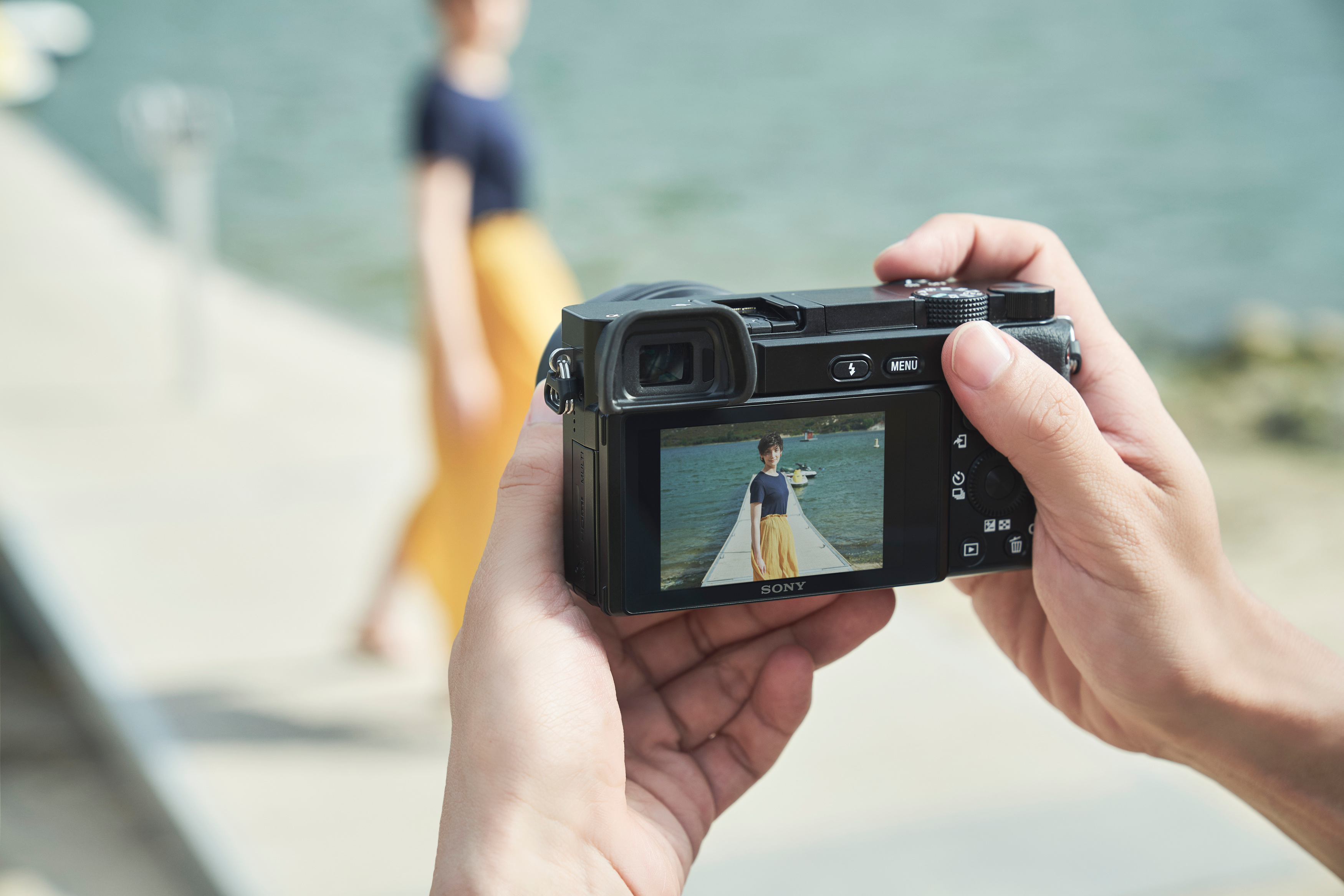 Person fotografiert andere Person auf einem Steg, reflektiert auf dem Kamerabildschirm.