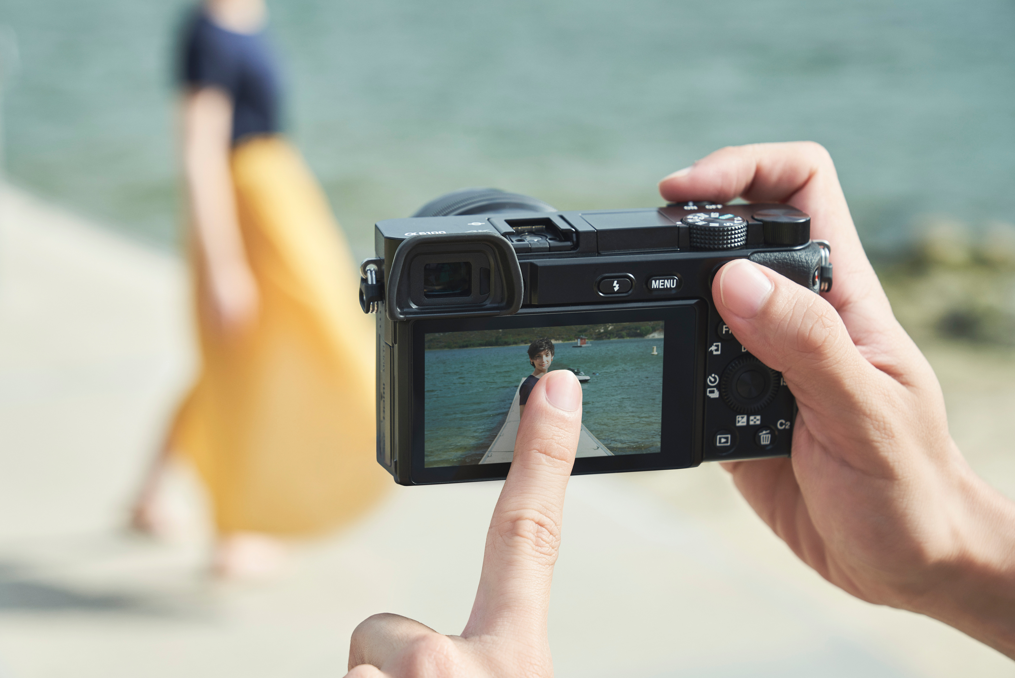 Person macht Foto mit Kamera. Person in gelbem Kleid im Hintergrund.