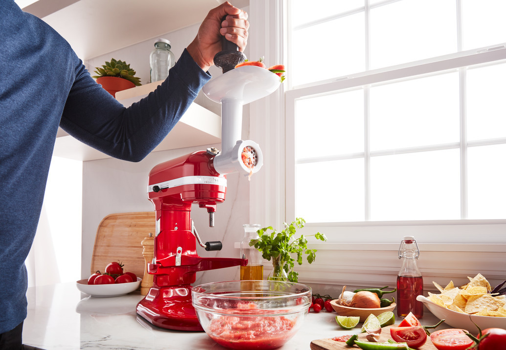 Person zerkleinert Tomaten mit roter Küchenmaschine in der Küche.