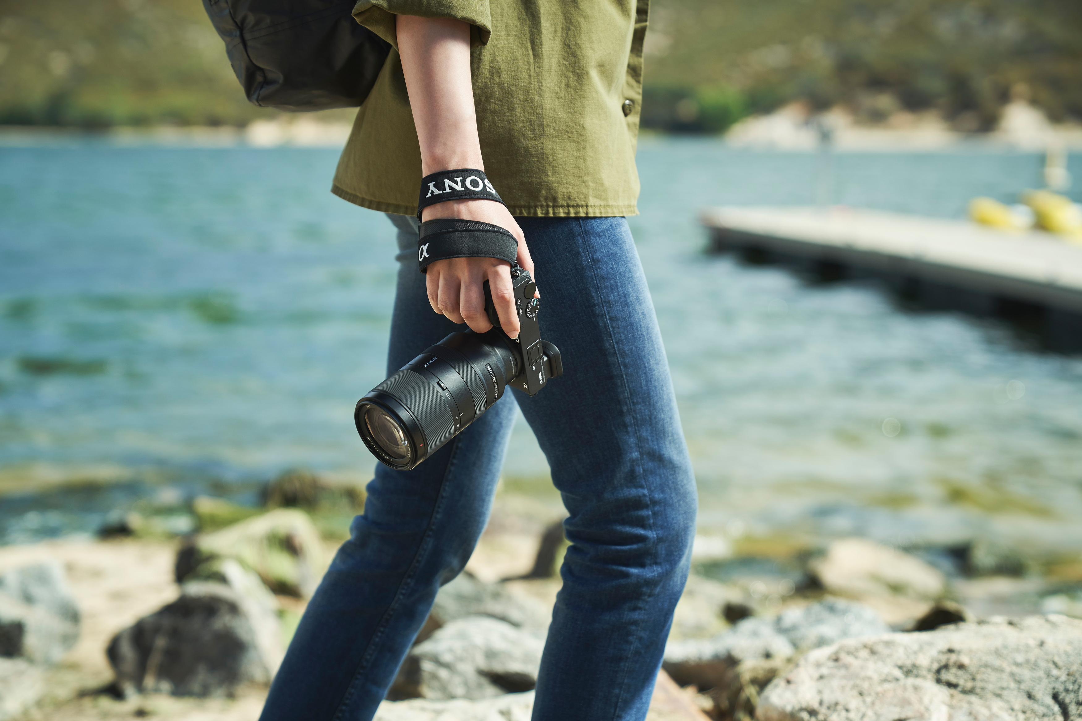 Person mit Jeans und grünem Hemd, die eine Kamera am Wasser hält.