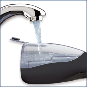 Ein Wasserhahn gießt Wasser in ein schwarzes Gerät. Das Gerät hat einen transparenten Bereich, der sich mit Wasser füllt.