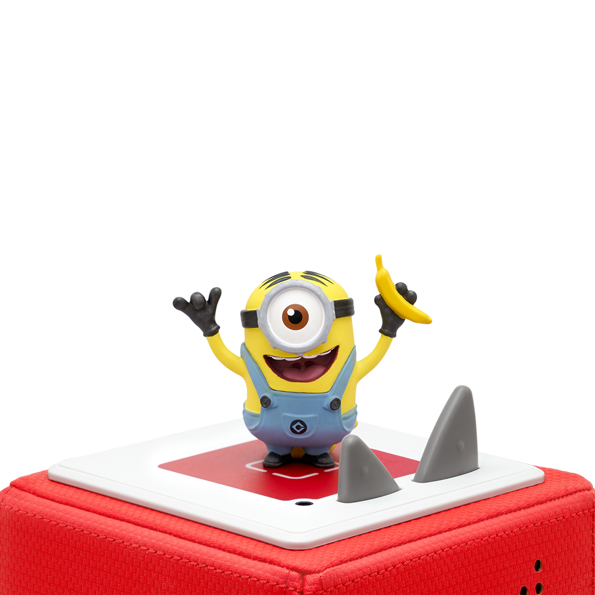 Ein gelbes Minion-Spielzeug mit einer Banane auf roter Oberfläche, mit Haifischflossen.
