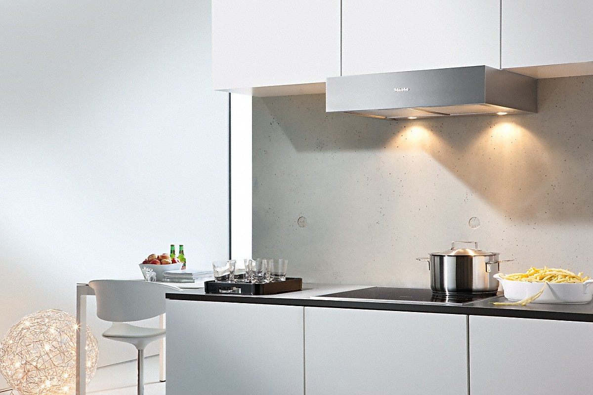 Cocina moderna con gabinetes blancos, una placa de cocina y una campana extractora plateada. Comida en la encimera.