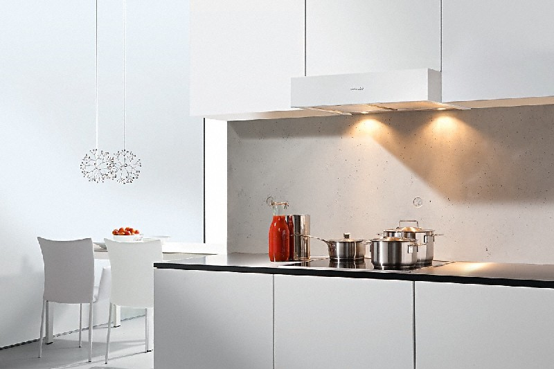 Una cocina blanca con campana extractora, estufa, ollas y una botella de jugo rojo.