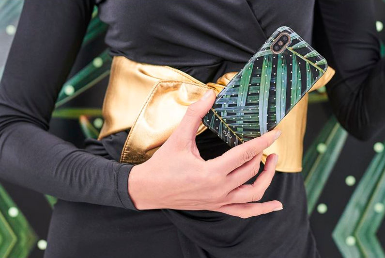 Een hand die een telefoonhoesje met een palmbladontwerp vasthoudt, met een gouden riem.