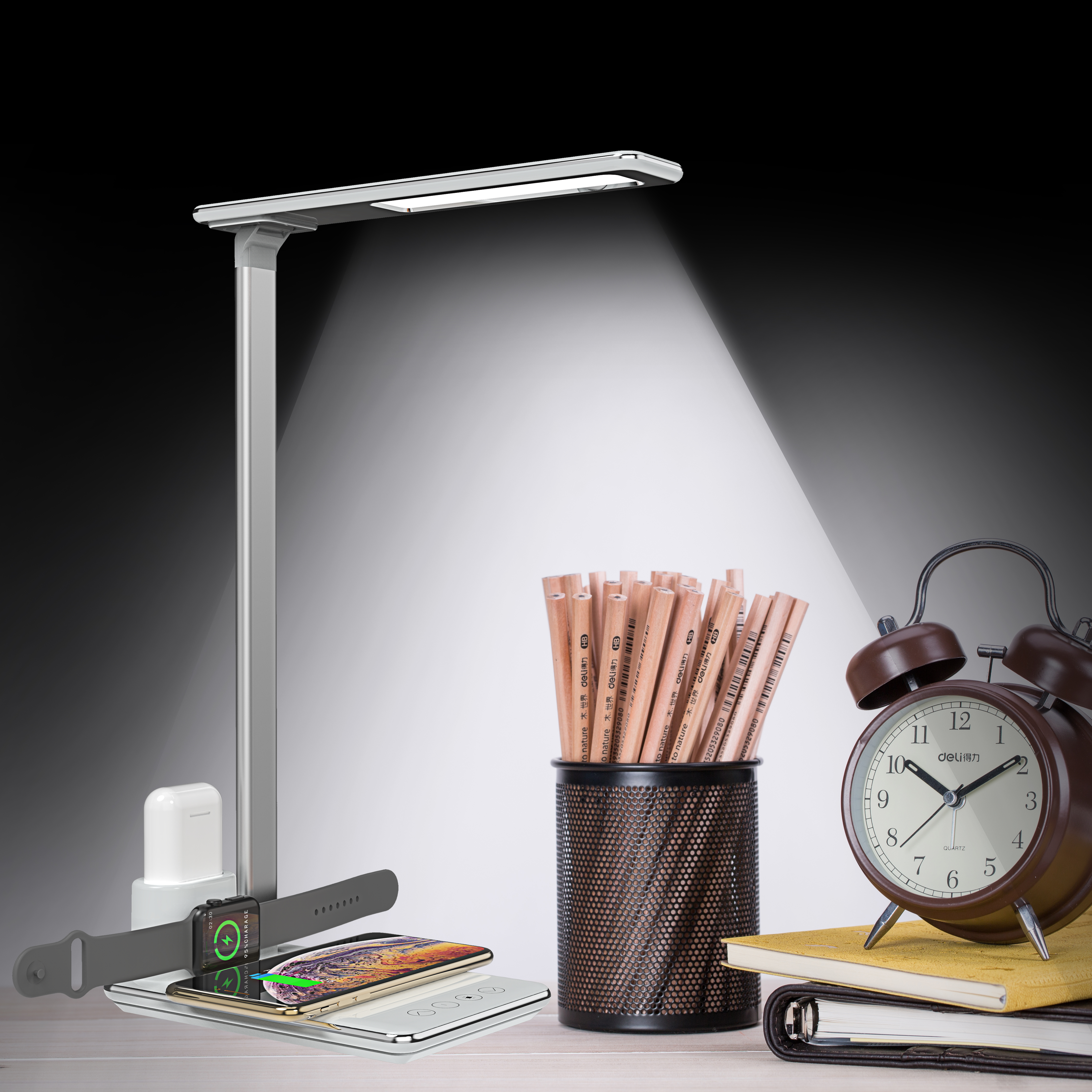 Schreibtisch mit Lampe, Ladepad, Bleistiften, Wecker und einem Buch. Licht auf den Bleistiften.