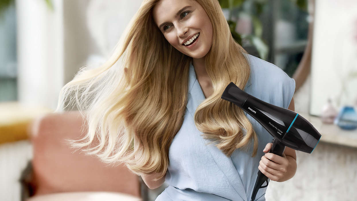 A woman is drying her long blonde hair with a Philips hair dryer.