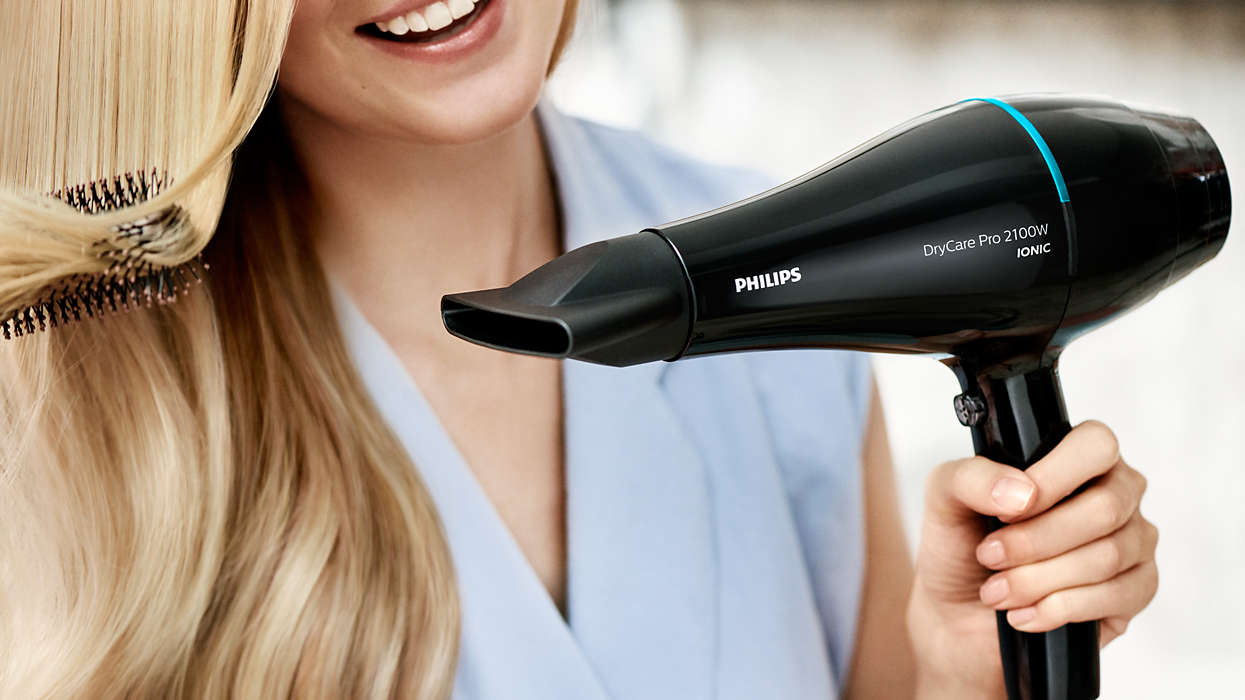 Woman using a black hair dryer on blonde hair.