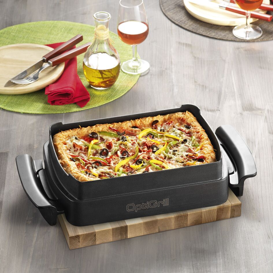 A rectangular pizza is in a grill pan on a wooden board.