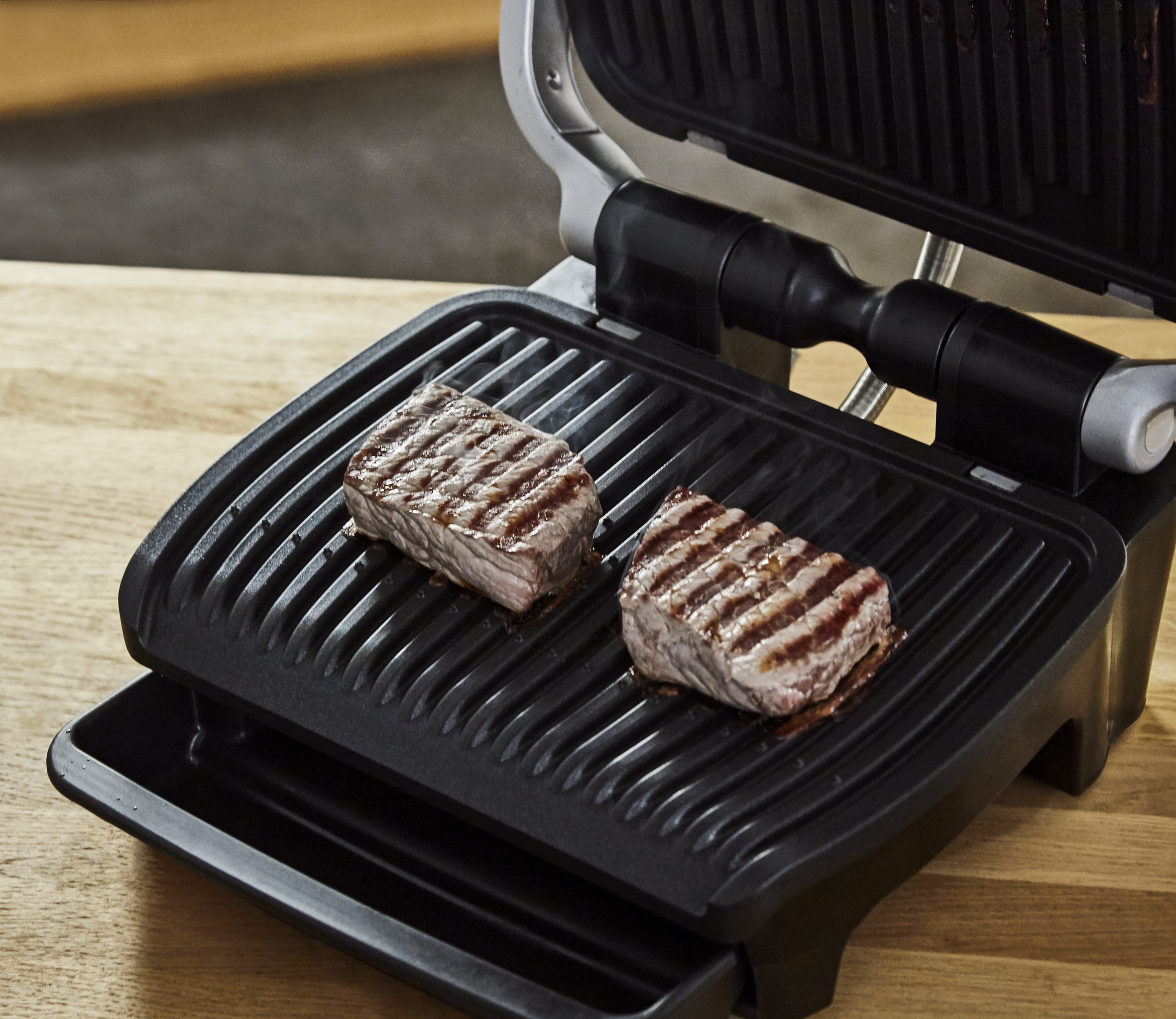 Binnengrill met twee gegrilde steaks, met grillstrepen, op een houten oppervlak.