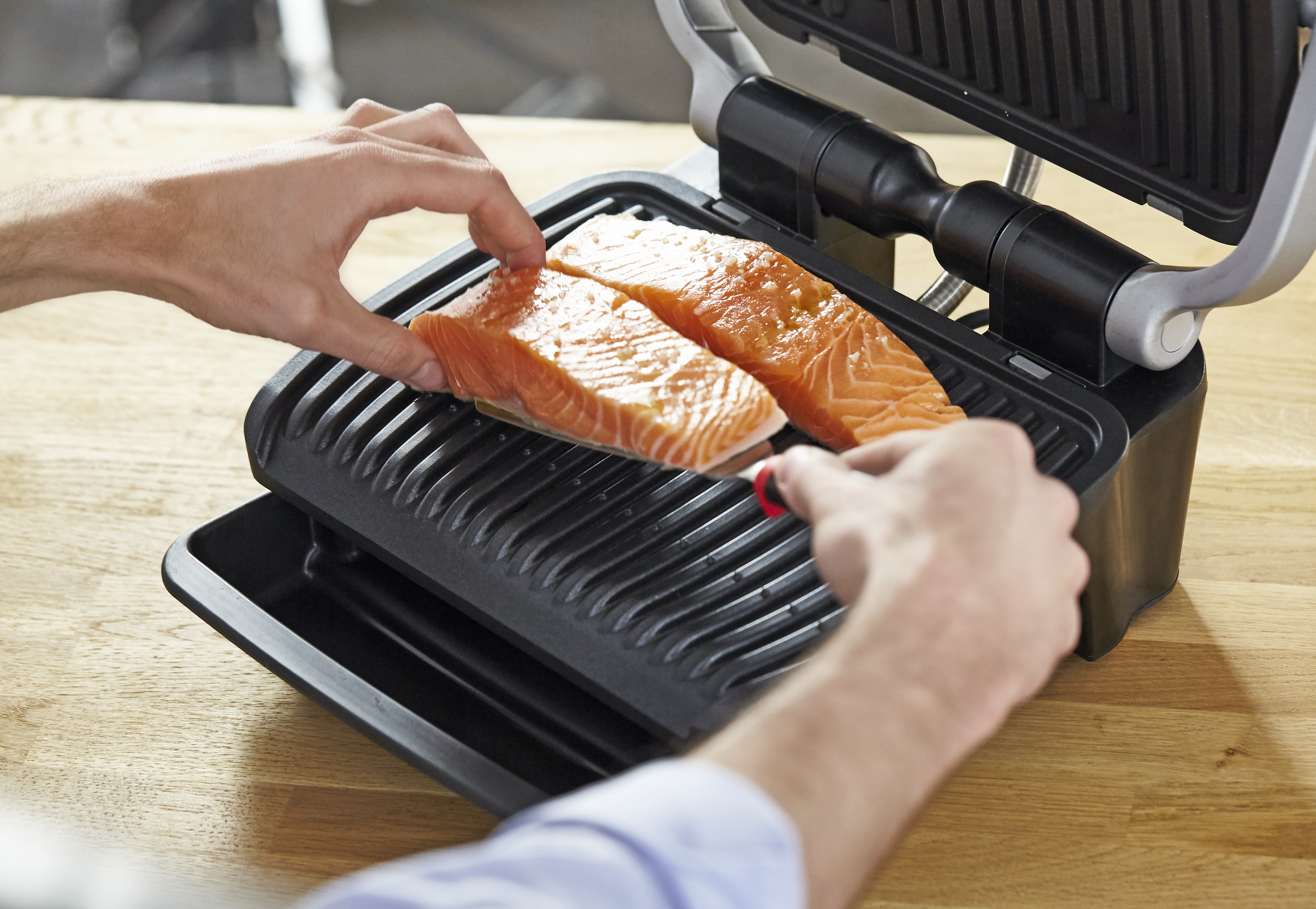 Handen plaatsen zalmfilets op een grill. De grill staat op een houten oppervlak.