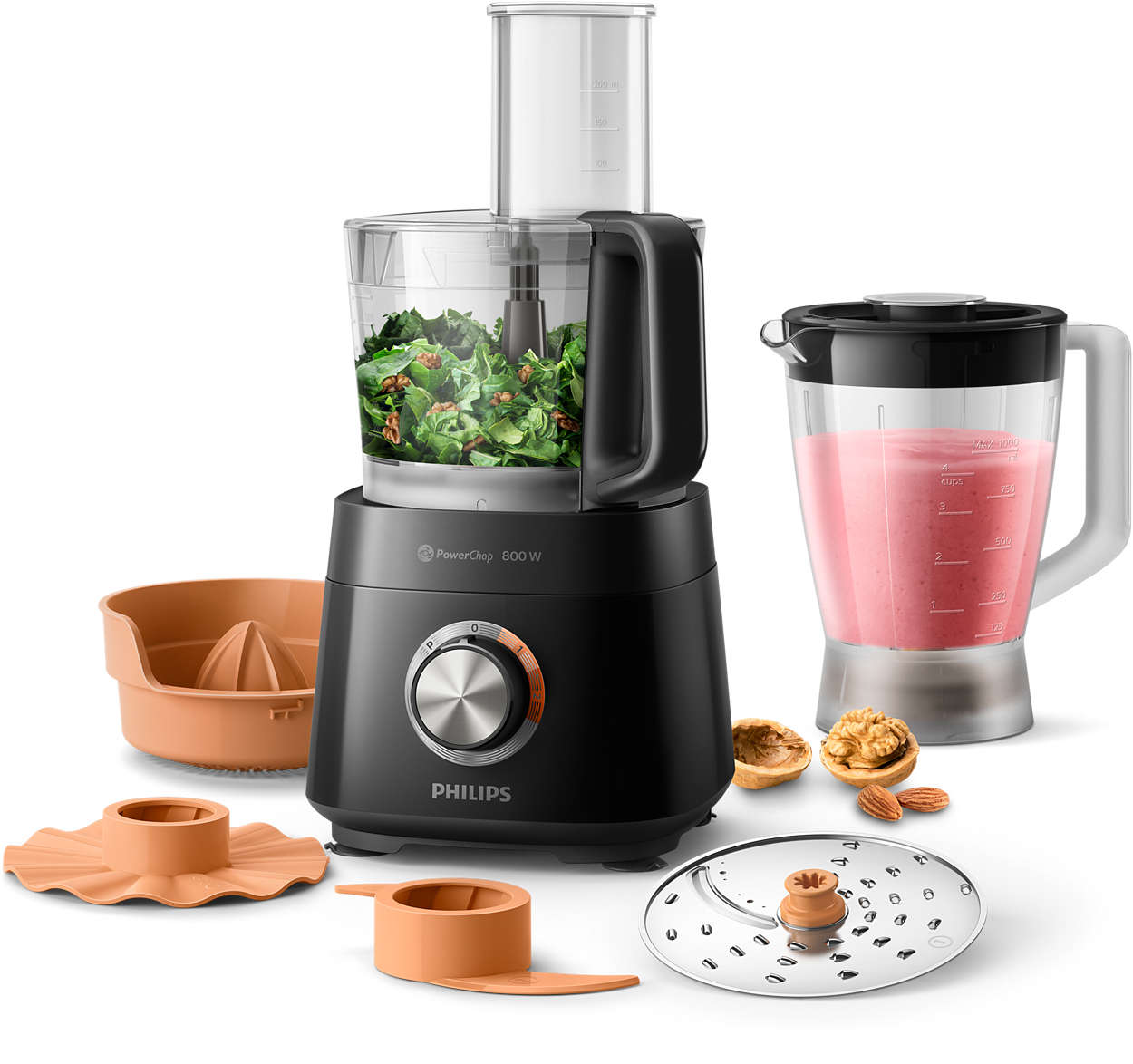 A black Philips food processor with attachments and ingredients like walnuts and greens.