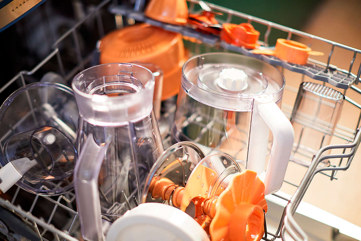 Dishwasher interior with orange and clear plastic parts. Jars, lids, and other kitchen tool parts are placed inside.