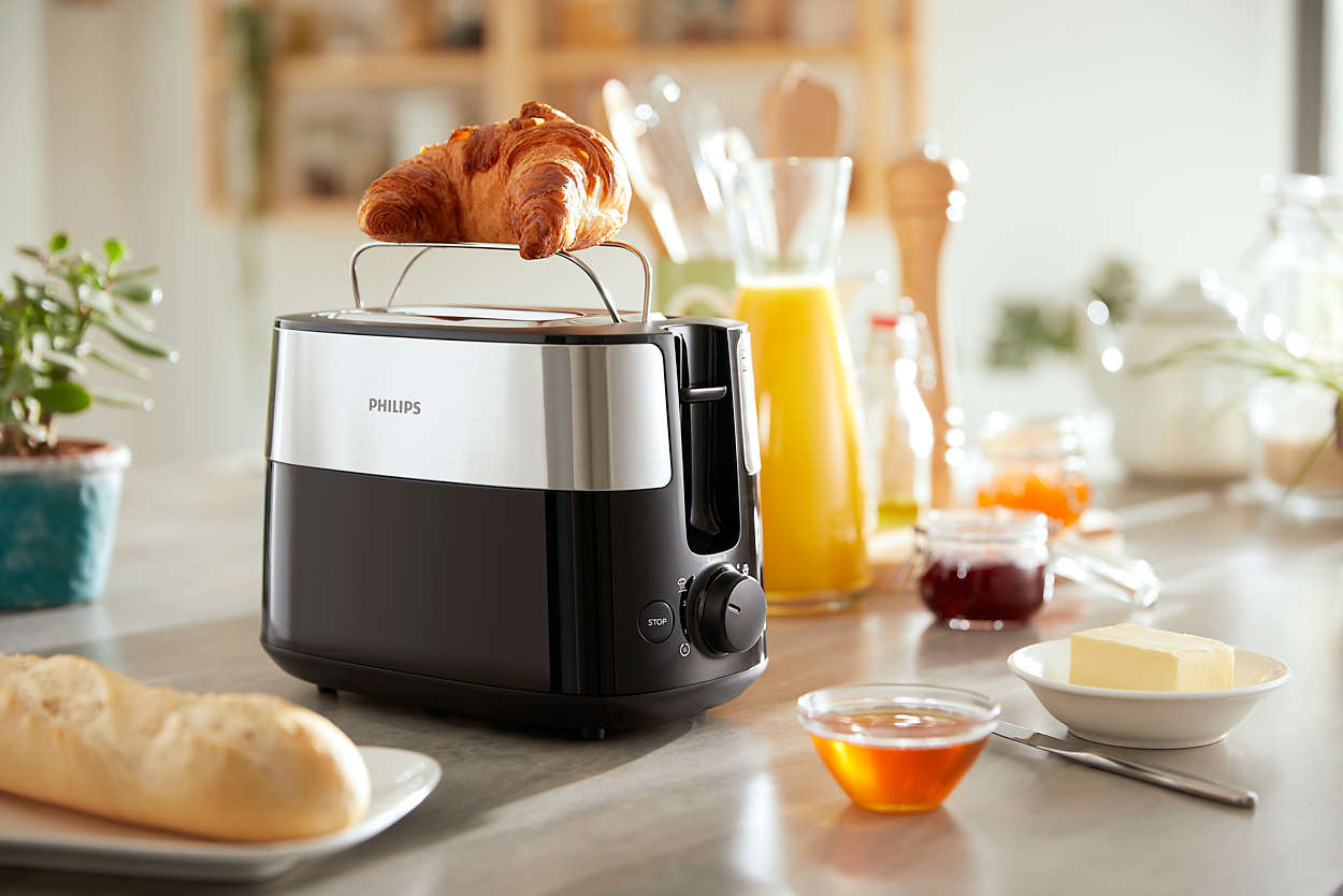 Toaster mit Croissant. Marmeladengläser, Saft und Butter auf einem Tisch. Frühstücks-Arrangement.